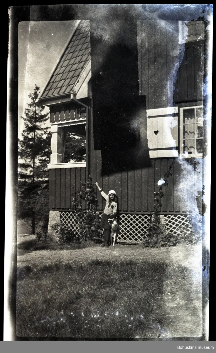 En person och en hund ståendes framför ett hus.