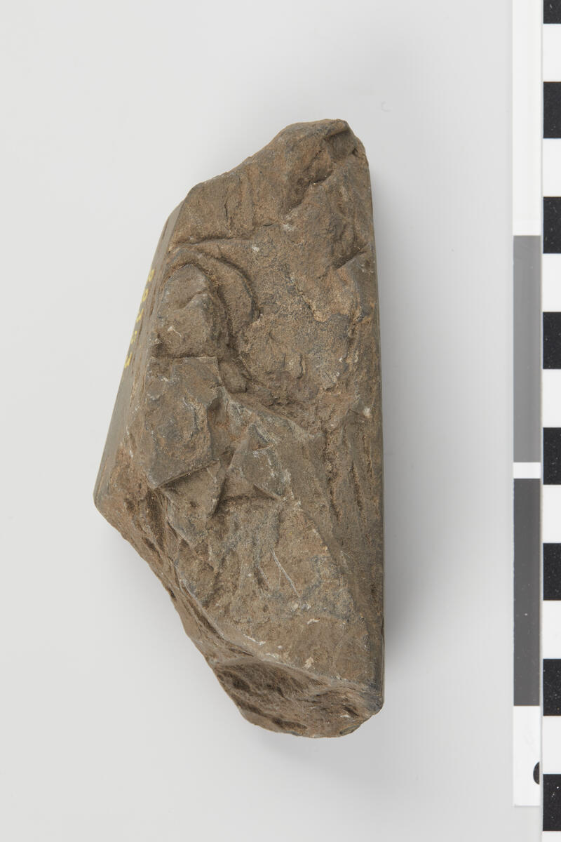 Et fragmentarisk stenstykke av nærmest tresidig form med rektangulært tversnit. Spor efter slipning paa tre av sidene. Længde 10,2 cm.