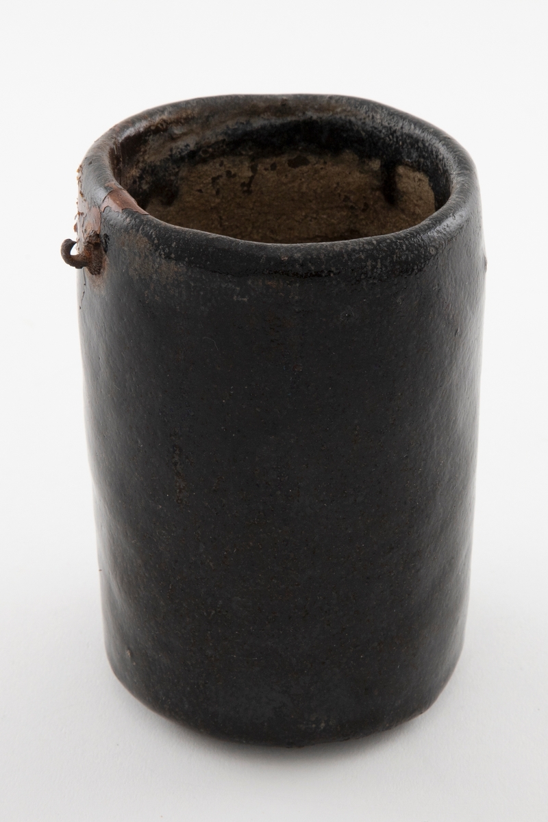 Vase i glasert keramikk. Vasen har ujevn flate, mulig håndformet, og er glasert i sort. Uglasert på innsiden. I øvre del, på utsiden, finnes en liten metallring, antakelig til oppheng.