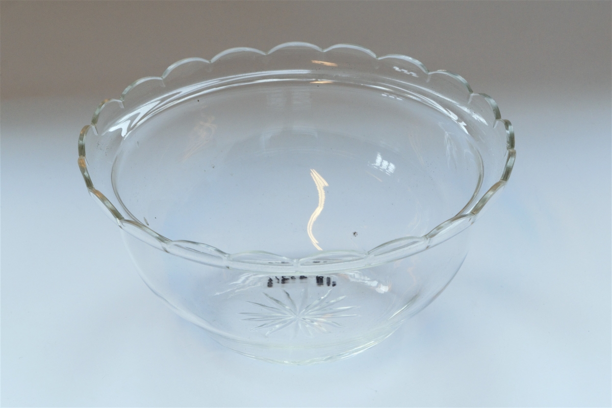 Skålformet potteskjuler i to deler. Den ytre delen er av sølvplett og den indre er av glass. Amerikansk design. Presset blomstermønster langs kanten av sølvskålen. Glasskålen har slipt stjernemønster i bunnen og dekorativ bord langs kanten.