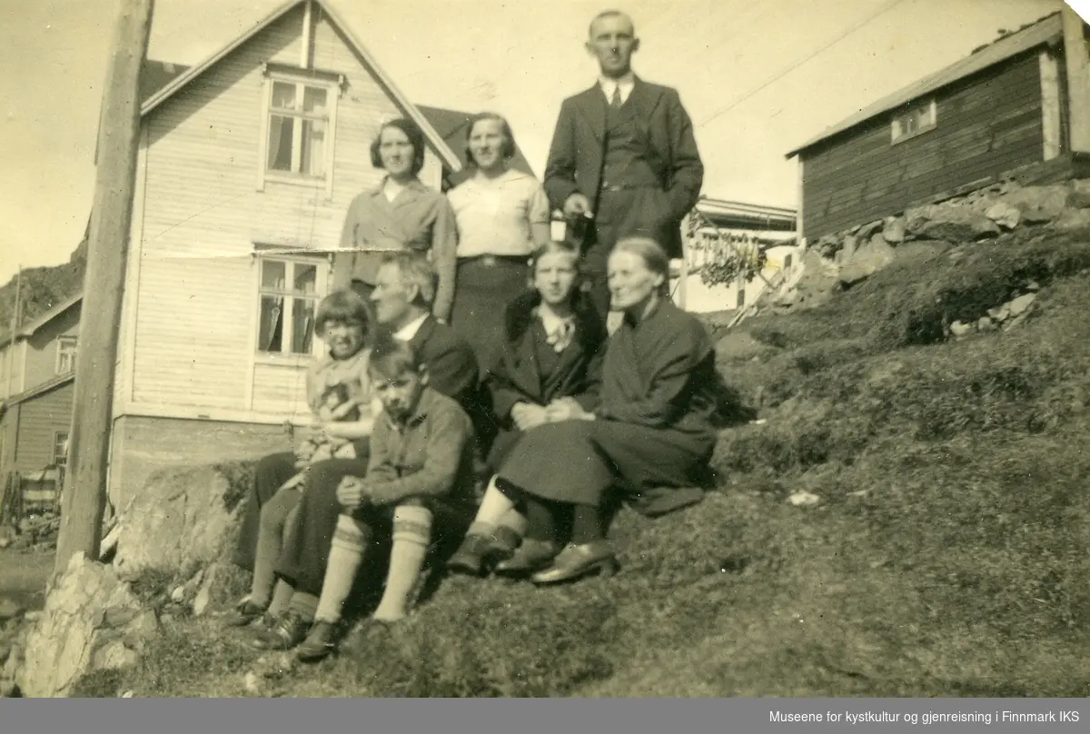 Honningsvåg, Holmbukt. Familien Svane utenfor familiens gård. I bakgrunnen tørrfisk på en hjell. Midten av 1930-tallet.