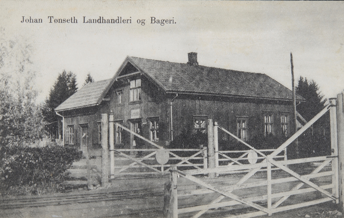 Postkort, Vang, Hjellum, Johan Tønseth landhandleri og Bakeri, planovergang med grind i forgrunnen ved Hjellum stasjon, senere bygde Tønseth slakteri og pølsemakeri på tomta,