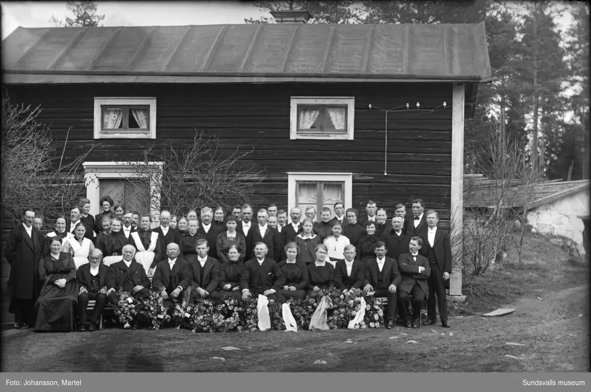 Gruppbild i samband med begravningen av Ernst Johansson som avlidit i spanska sjukan endast 21 år gammal. Ernst var bror till fotografen Martel Johansson och hans syskon. Fotot taget framför bruksstugan på gården Brännsvedjan i Sörfors.