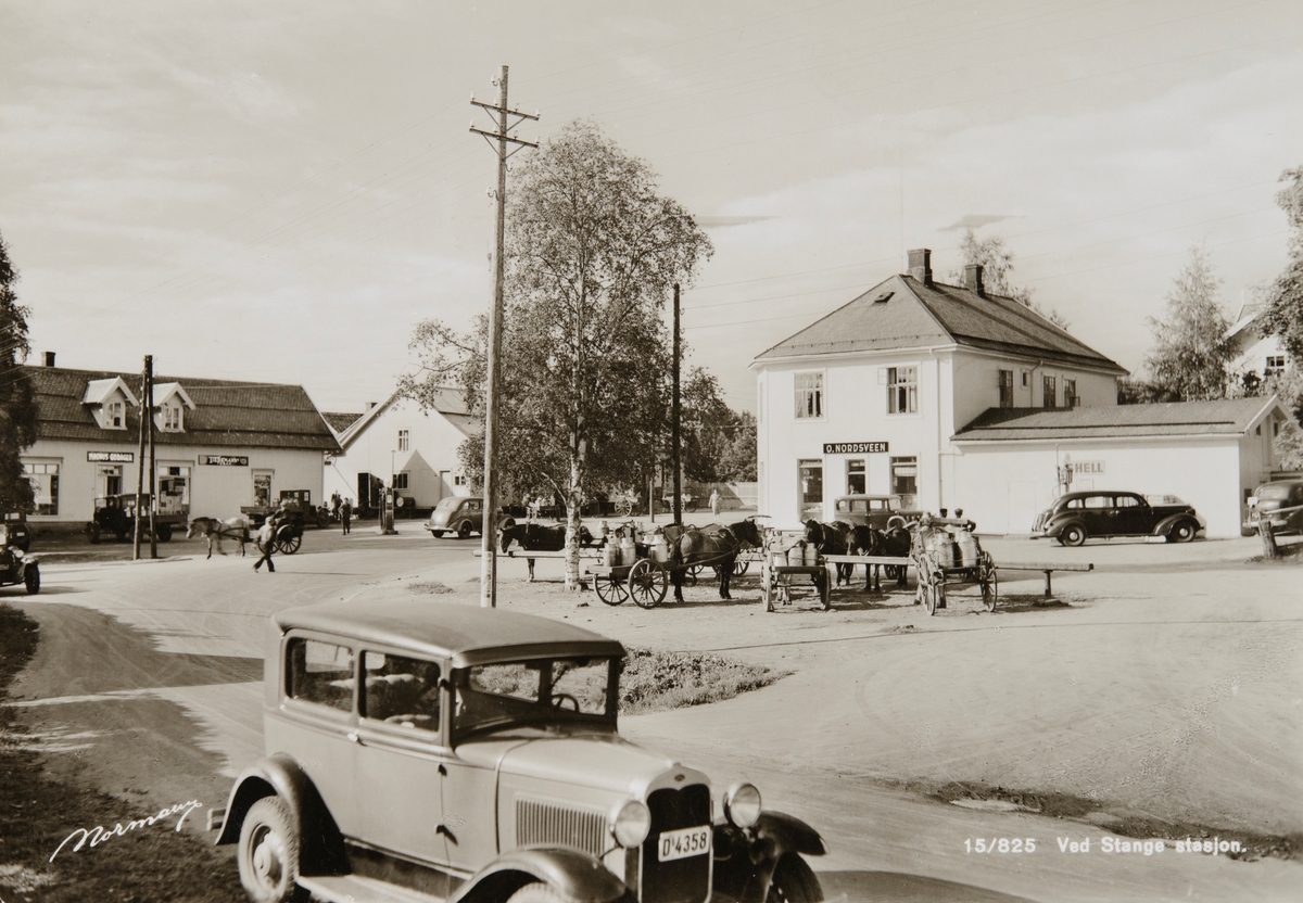 Postkort, Stange sentrum, Stangebyen, fra venstre: Magnus Godagers forretning i Storgata, og O, Nordsveens butikk til høyre, hestebinding på meieritorget, hester med stuttkjerrer kjører mjølk, en bil: Ford i forgrunnen med registreringsnummer D-4358, i heftet Hedmarks Bileiere 1938 er den registrert på Ole Wie,