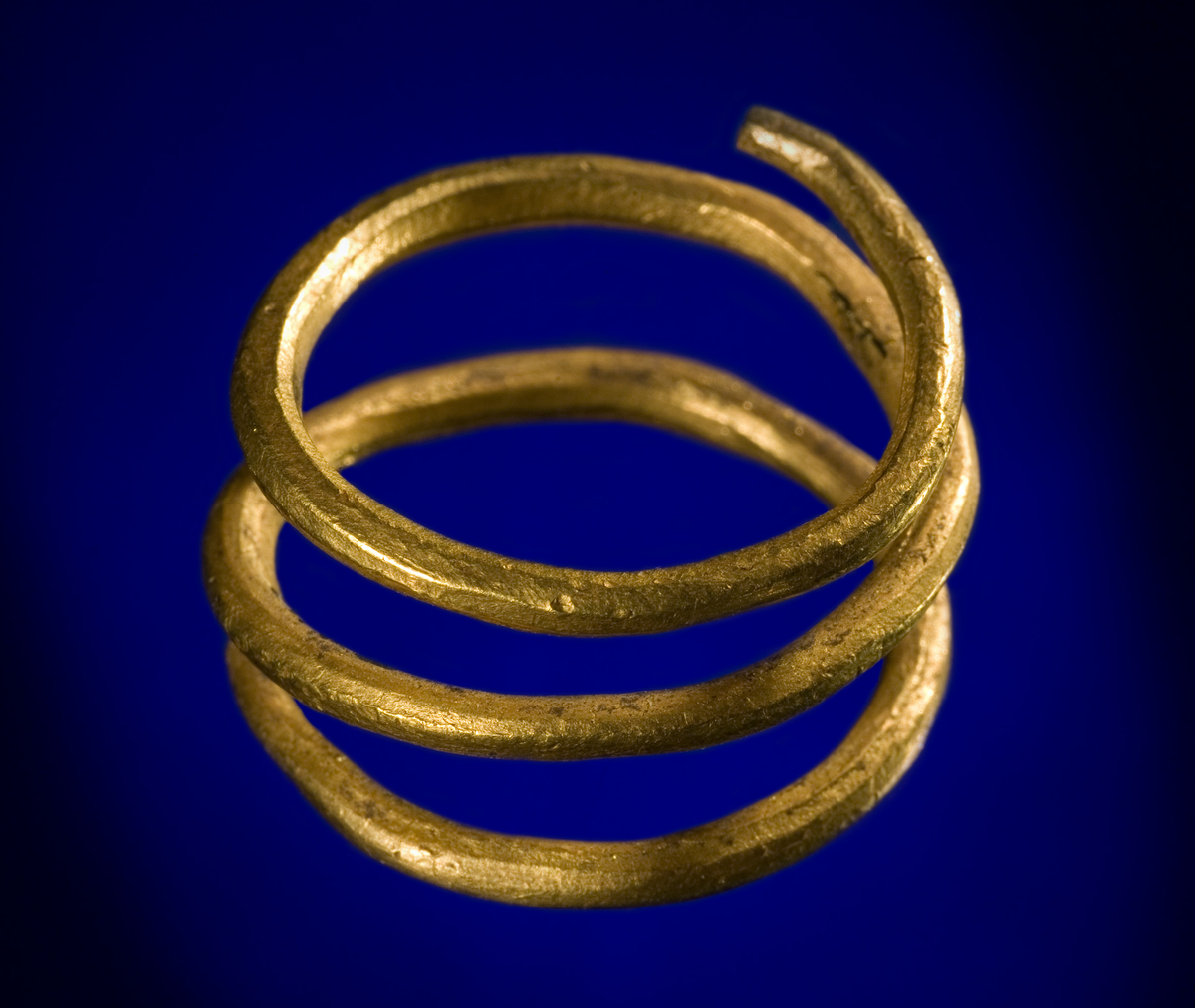 Spiralfingerring av guld av typen R. 183. Den adskiller sig fra typeeksemplaret ved at tenen er noe tynnere, og at den er snodd den andre veien. Tverrmål 2,3 cm, tenens tverrmål 0,15 cm. Vekt 11,85 gr.