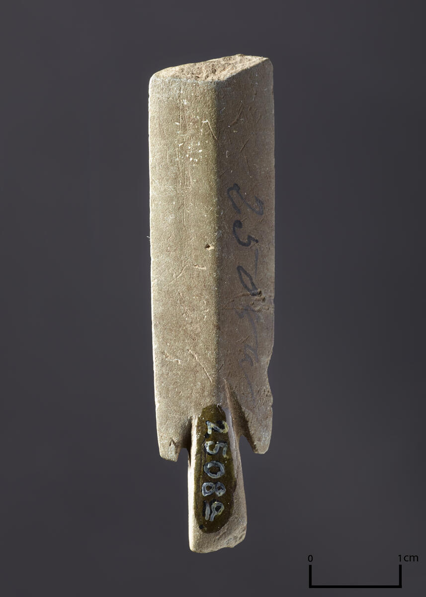 Stykke av en pilespids av skifer, lik "Den arktiske stenalder", fig. 72. 5,5 cm lang, hele den forreste del mangler.