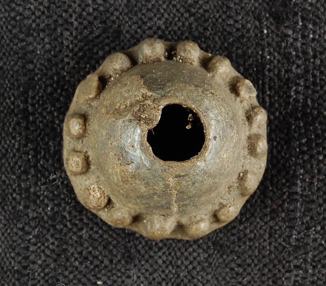 Konisk spinnehjul av bly, hvor den nedre halvdelen er dekorert med tettstilte stående ribber/riller. Det har en høyde på 1,42 cm, diameter på 2,37 cm og hullet har en største diameter på 0,68 cm. Ligner Øye 1988 fig II. 14. Datering: slutten av 1200-tallet til 1400-tallet (Øye 1988, s. 50).