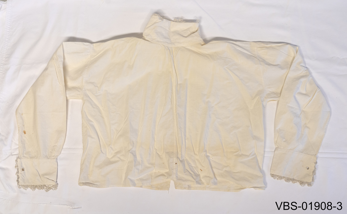 Hvit skjorte til bunad i bomull. Nupperellekant helt ytterst langs kantene på ermer og halslinning. To plastknapper dekket i  bomullsstoff.