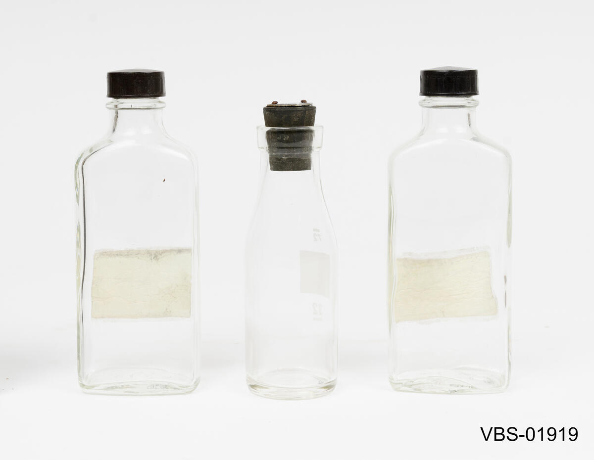 Laboratorieutstyr som består av 3 glassflasker laboratorie gjenstander av glass og en gummiproppen.
Gummiproppen har en rund aluminiumsplate spikret med to sifre: 77 

1 rund flaske med gummiplugg
2 flate flasker med skrukork