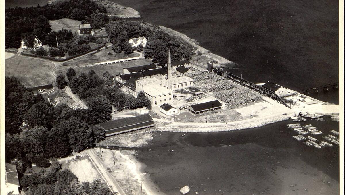 Sort-hvitt-bildet viser et fabrikkområde som ligger rett ved sjøen