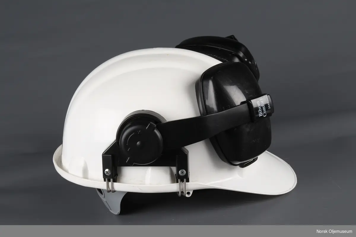 Vernehjelm med påmontert hørselsvern. Hjelmen har et klistremerke med Norwegian Contractors sin logo foran.