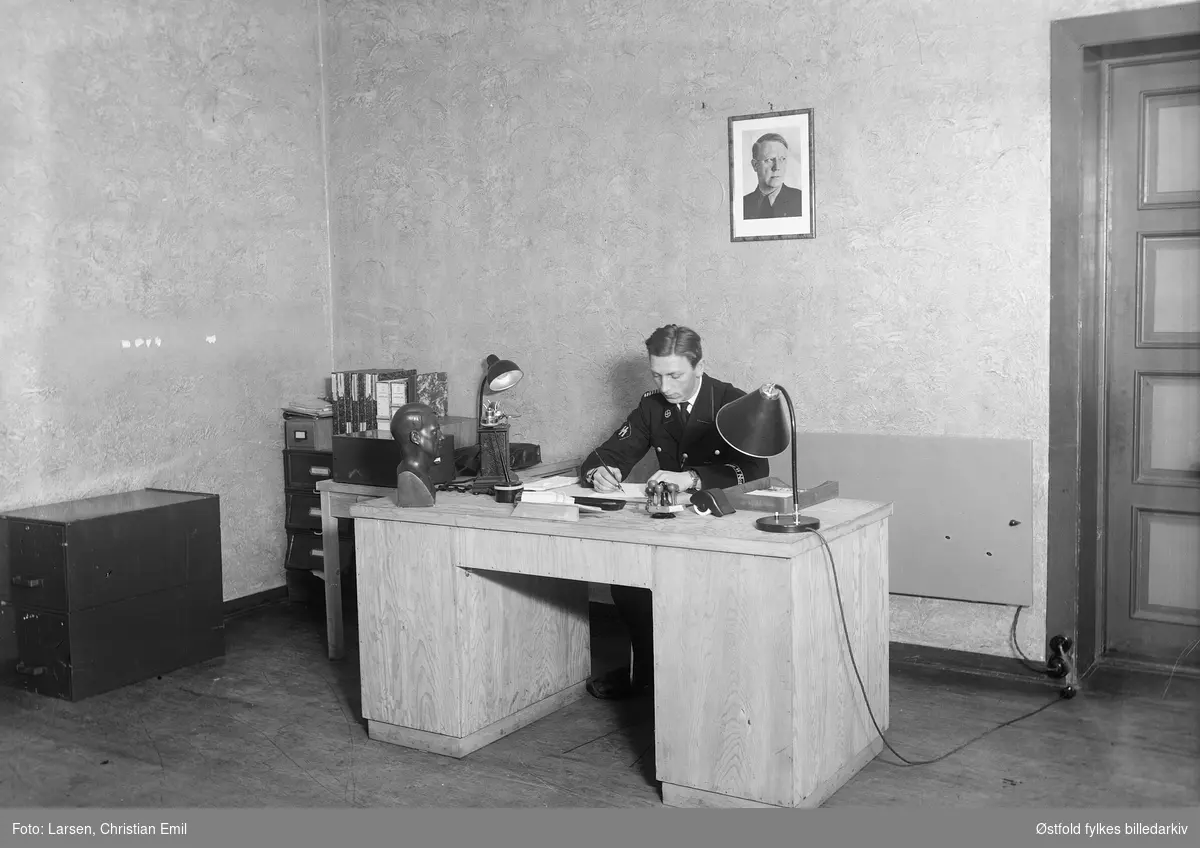 Ukjent mann i uniform, kontorinteriør, 1942-43.  På uniformsarmen: Germanske SS Norge. På bordet byste av Vidkun Quisling. På veggenportrett av Vidkun Quisling.