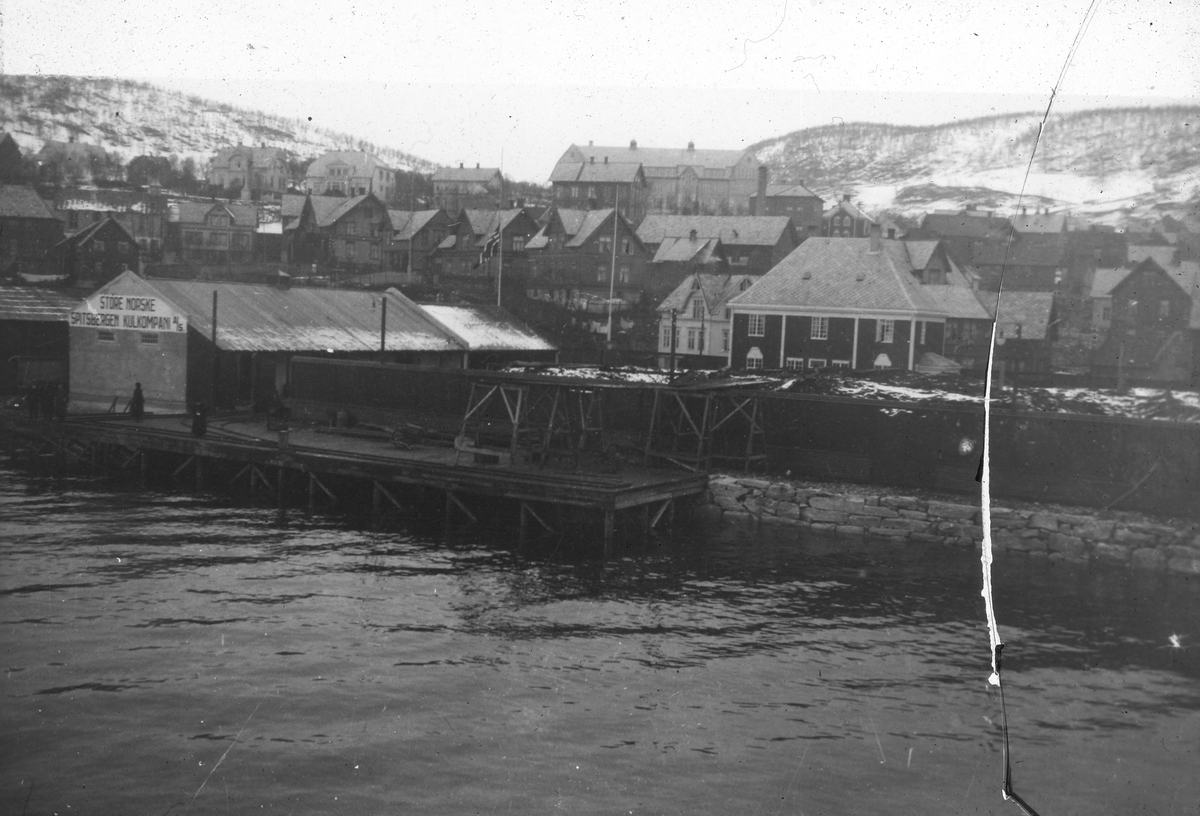 Havneområdet i Harstad i 1920. På skiltet på bygningen til venstre står det,Store Norske Spitsbergen Kulkompani A/S. Tekst med bildet: 1920  Harstad-avdelingen. Bildet er sprukket.