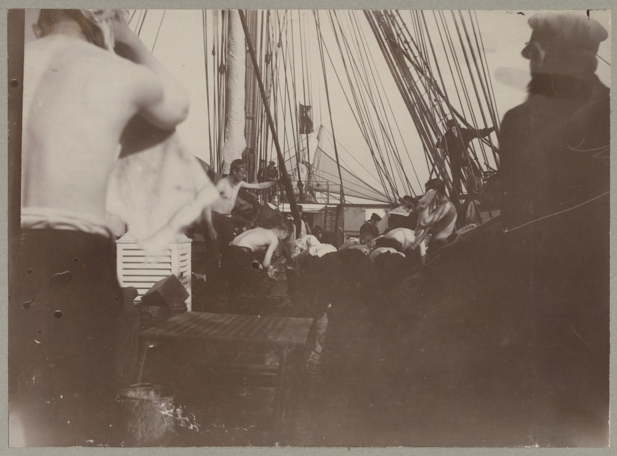 En grupp sjömän med bar överkropp tvättar sig på däcket. I förgrunden torkan en man håret med en handduk.