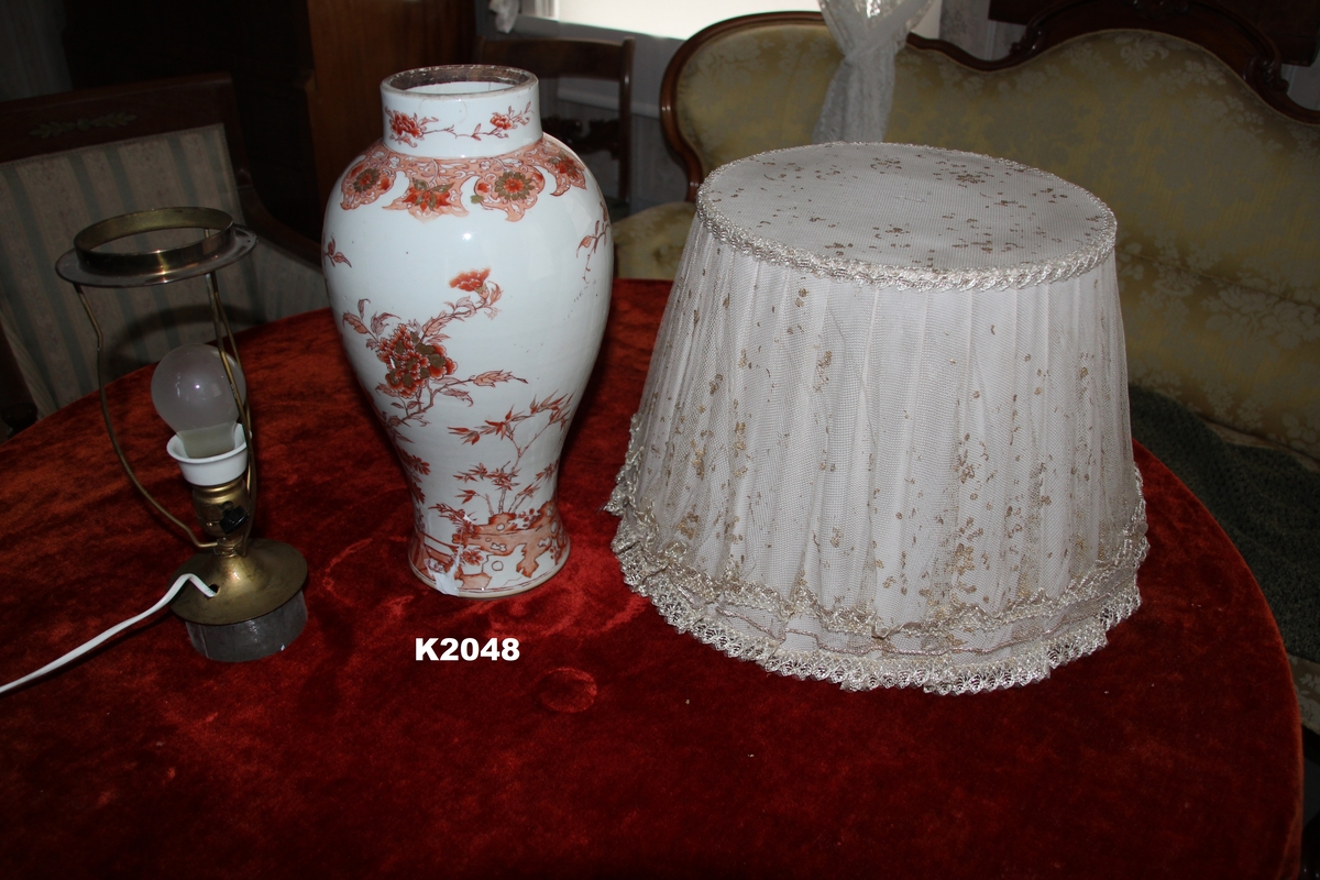 Vase montert som lampe: Porselen, antagelig japansk. Med malt blomsterdekor i jernrødt og gull på hvit bunn.
Skjerm: Moderne, blek rosa silke med tyll over.
Lampen: Laget av messing med holder for pære laget av kjeramikk.