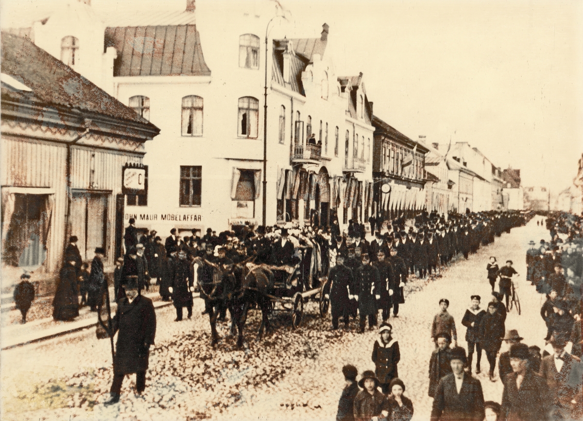 Storgatan, Växjö, 17 oktober 1916, i korsningen mot Bäckgatan. Biskop Lindströms begravning.
Man är på väg till gravsättning på Tegnérkyrkogården. Likvagnen är omgiven av en hedersvakt av Växjös poliser.