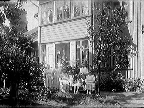 Gruppbild av människor utanför en villa. Möbelhandlare C J Carlsson beställde bilden och är troligen själv med.