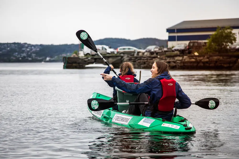 To jenter på vei ut av havnen i en grønn kajakk, for å plukke søppel langs land i nærområdet