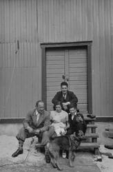 Gruppebilde av fem personer foran en låve med familiens hund