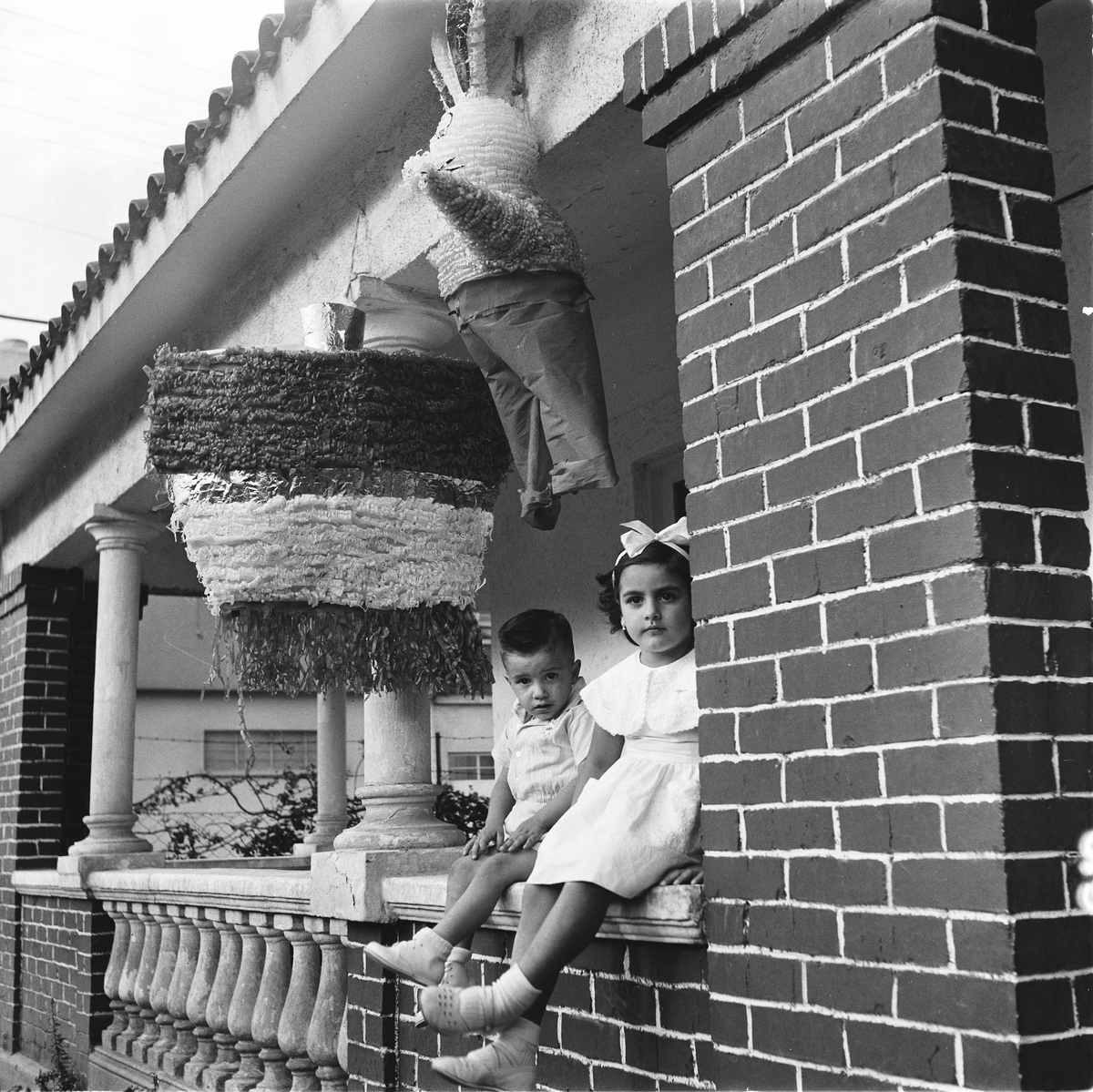 To barn sittende på veranda med piñata hengende over seg.