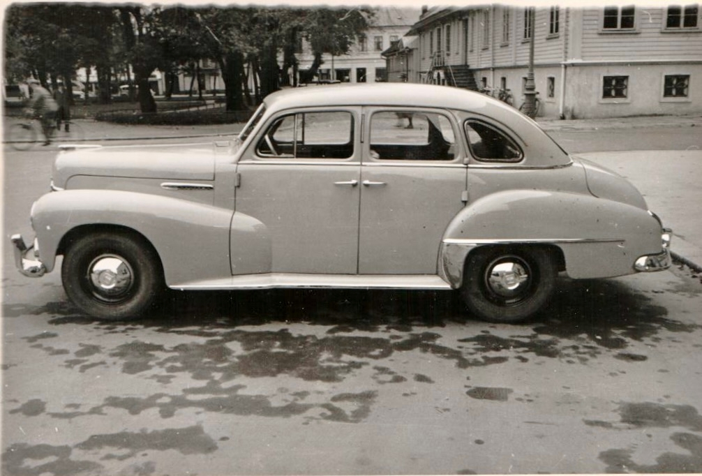 Sivil personbil av merket Opel Kapitän (årsmodell 1950-53) med registreringsnummer K-650 står parkert foran en bygning. Bilen er fotografert både forfra og fra siden.