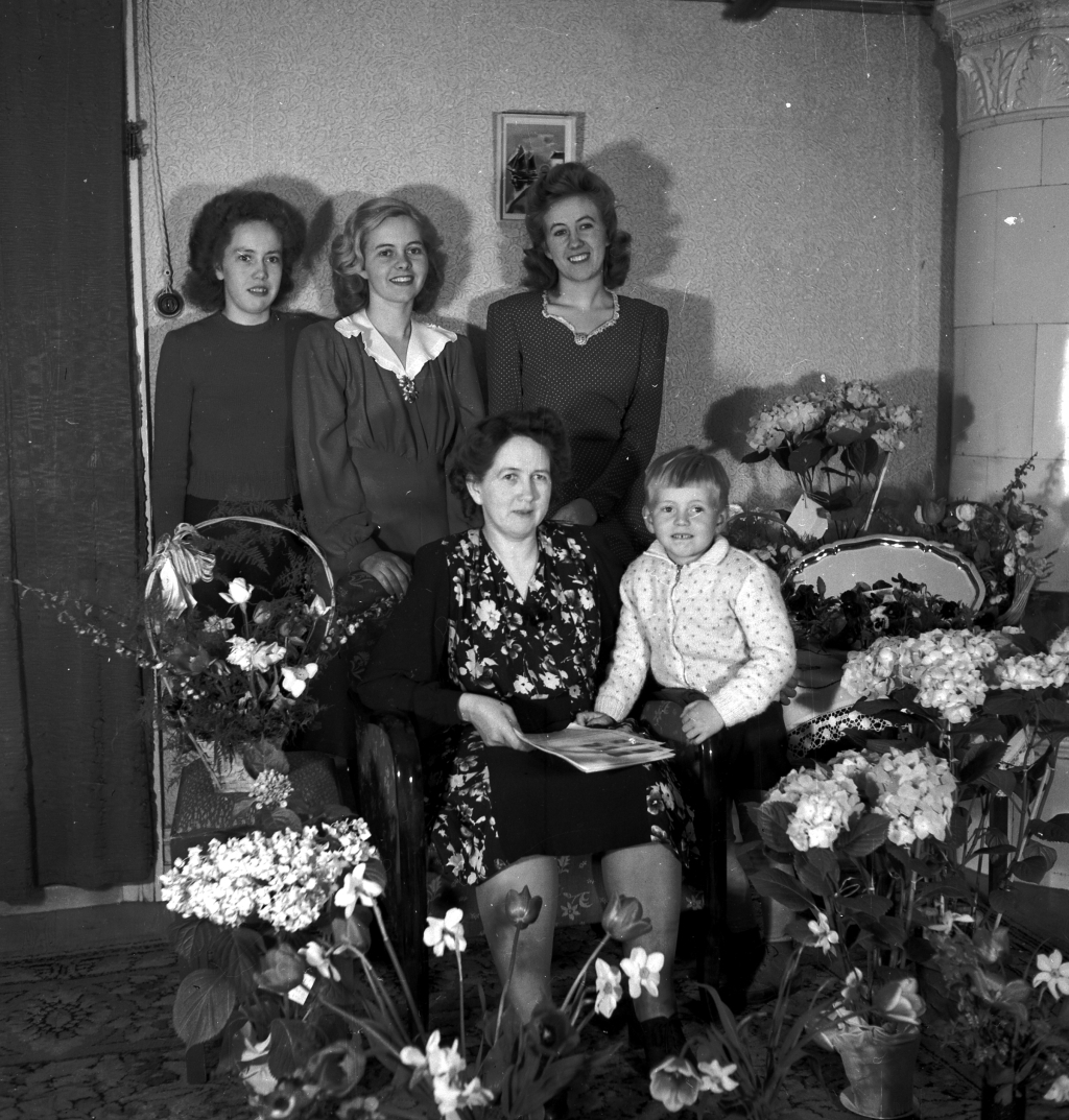 Fem personer samlade bland en mängd blomsterbuketter.