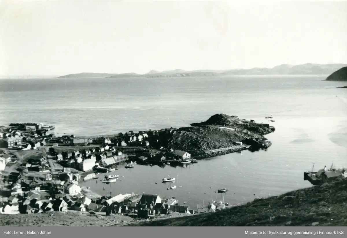 Honningsvåg. Oversiktsbilde tatt fra Storfjellet. Indre havn med bebyggelse. Helt til venstre ser man skolen, og til høyre dampskipskaia med et skip. 1939.