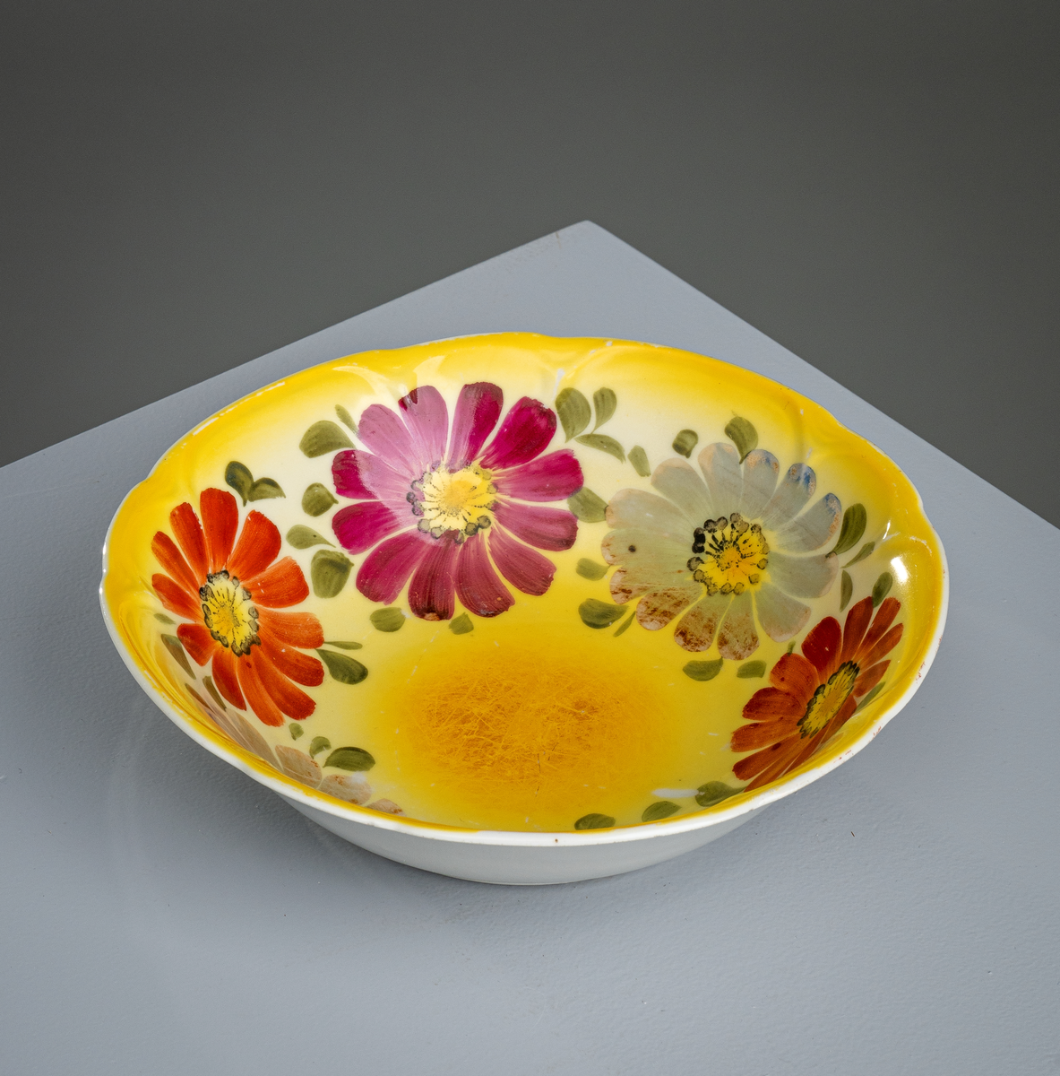 En suppebolle av keramikk/porselen. Den har klassisk "bolleform". Innvendig er den gul med påmalte blomster og blader. Det er ialt seks blomster (to rødoransje, to burgunderfargede og to grågrønne) med små brønne blader. Utsiden er hvitglasert.