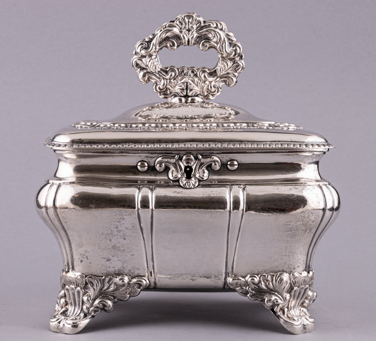 Sockerskrin av silver, fyrsidigt med lock på gångjärn, med nyckel. Uppstående ögleformigt handtag på lockets ovansida.
Stämplad:
E. G. Öström 
G.
V4