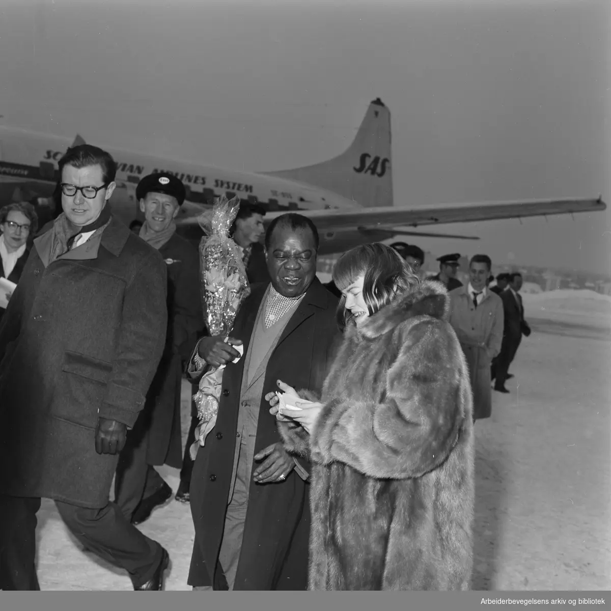 Louis Armstrong ankommer Oslo via Fornebu flyplass 2 februar 1959. Omgitt av journalister.