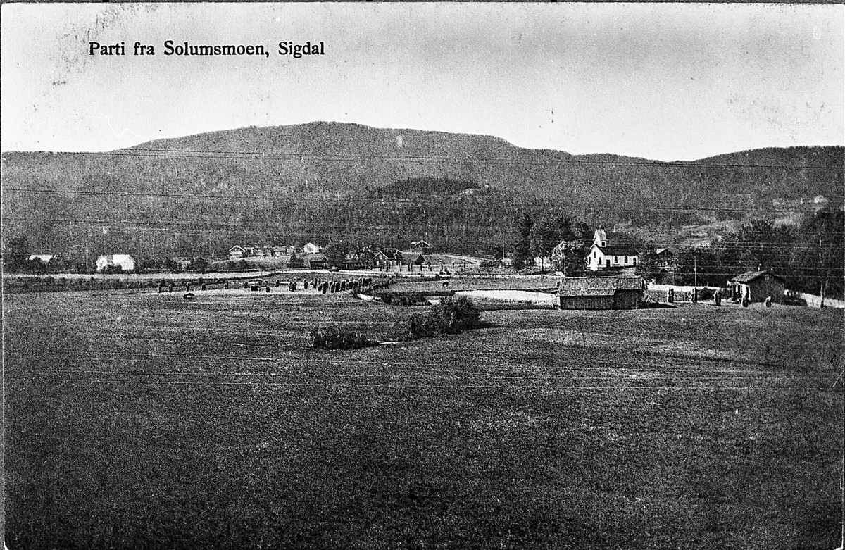 Utsyn over Solumsmoen, med flere gårder og Solumsmoen kapell. Udatert postkort, trolig rundt 1910.