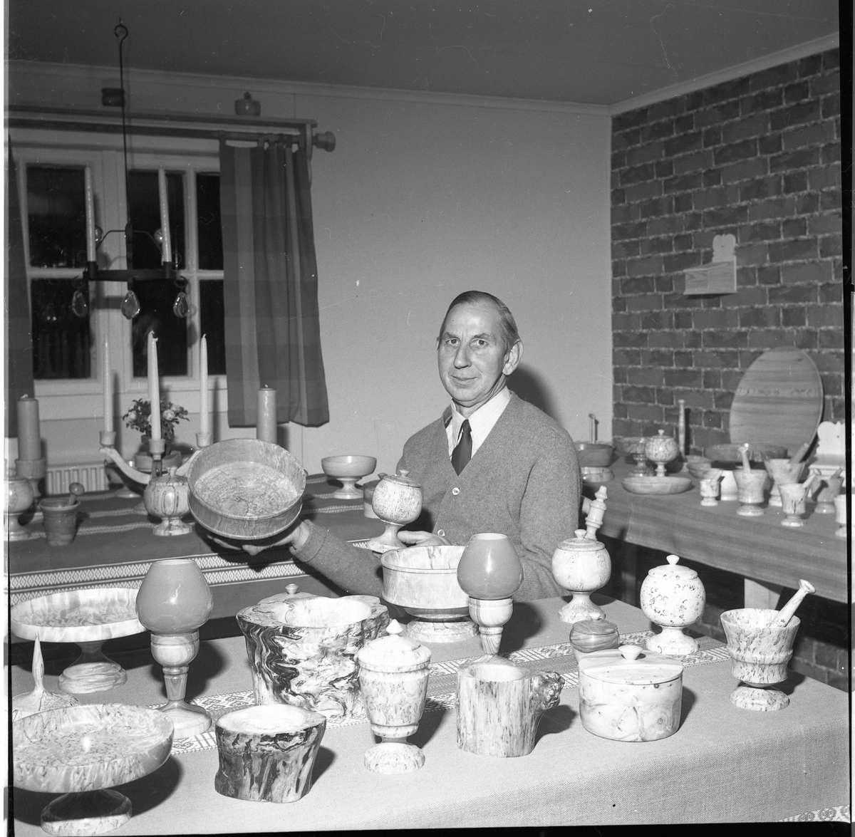 En man i cardigan vid ett bord med ett stort antal svarvade skålar och fat.