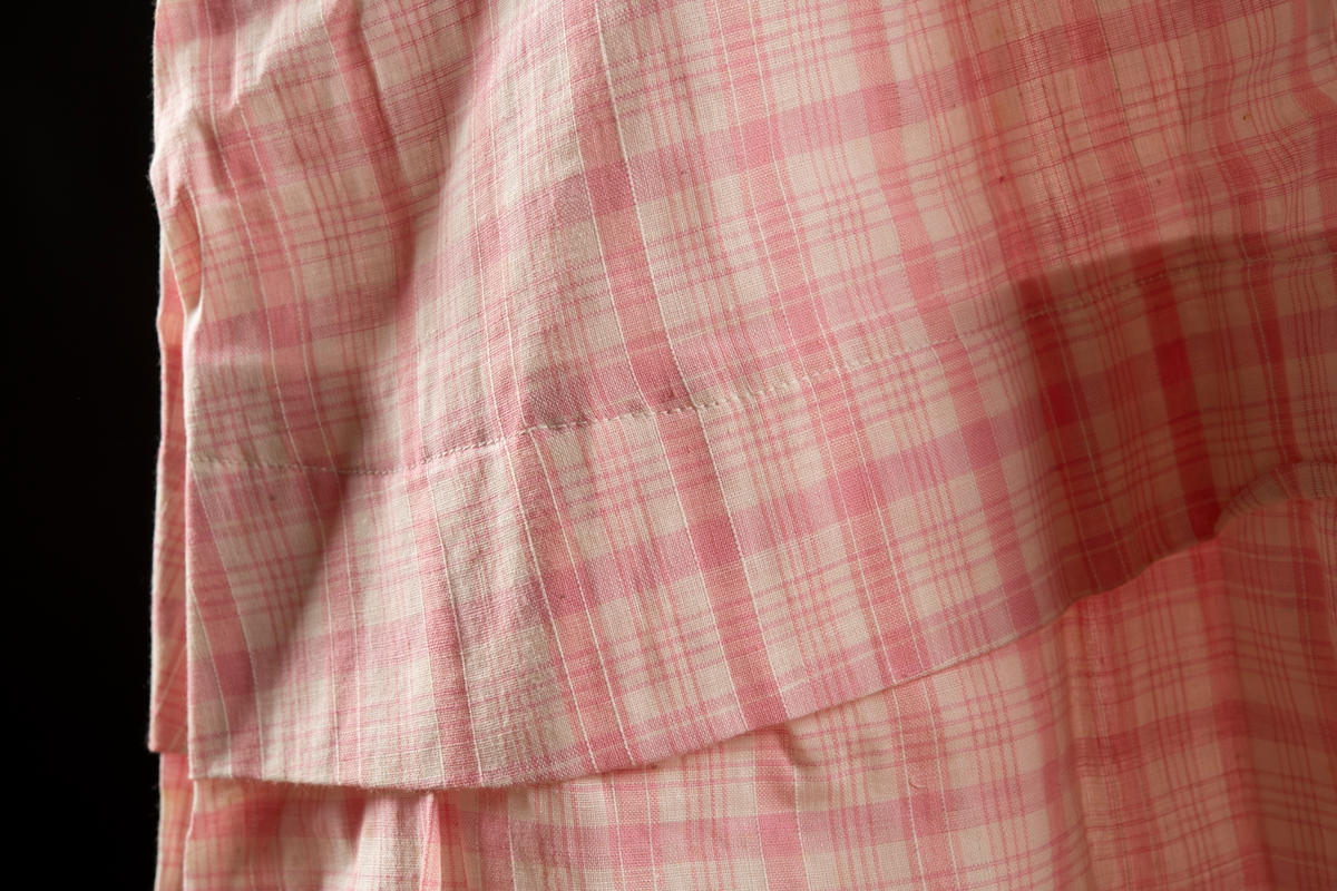 Kortärmad klänning av rosa rutigt tyg. 5 cm brett upplägg i knähöjd.