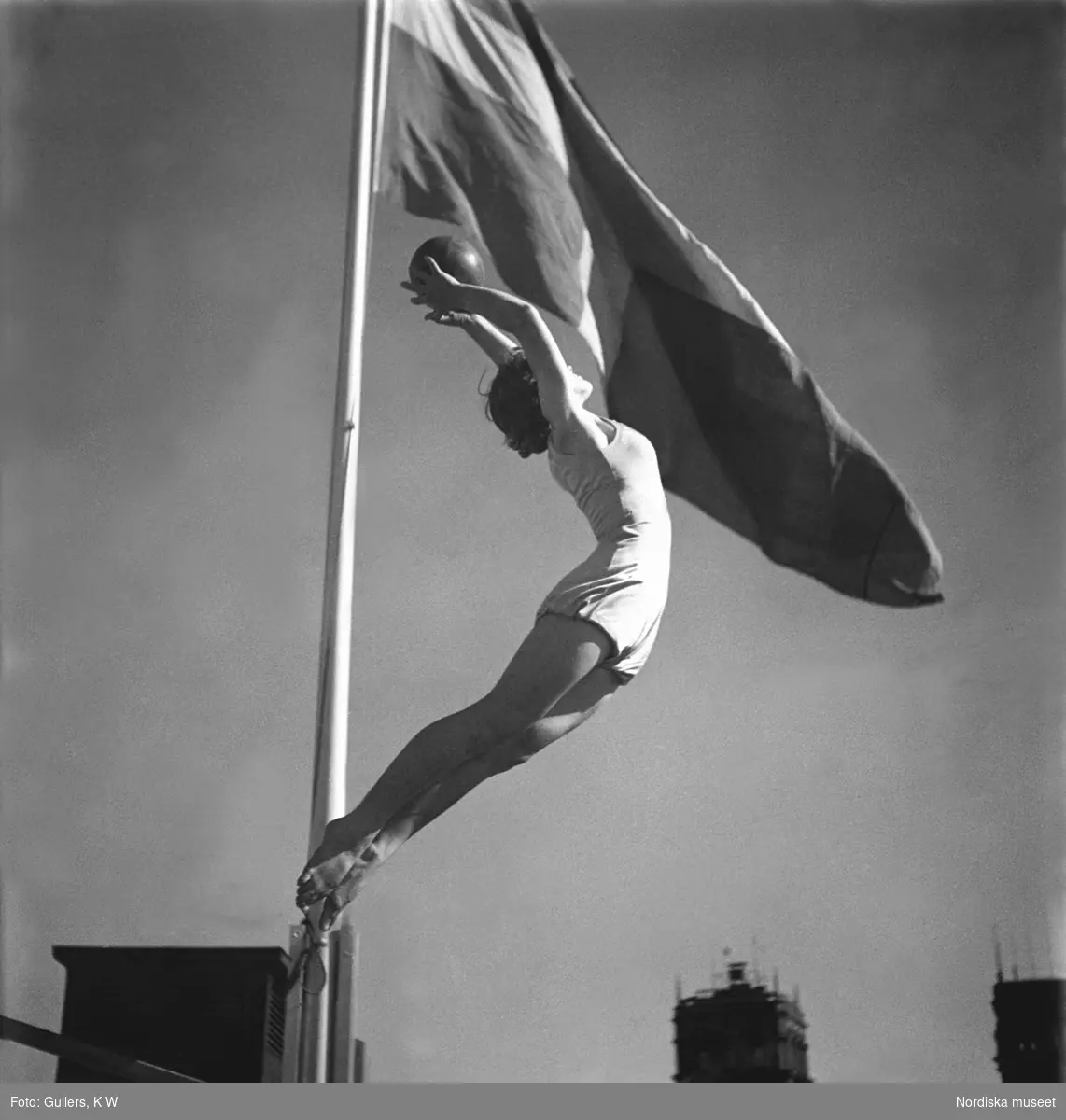 Gymnastiserande flicka med boll, med svenska flaggan i mörk bakgrund.
