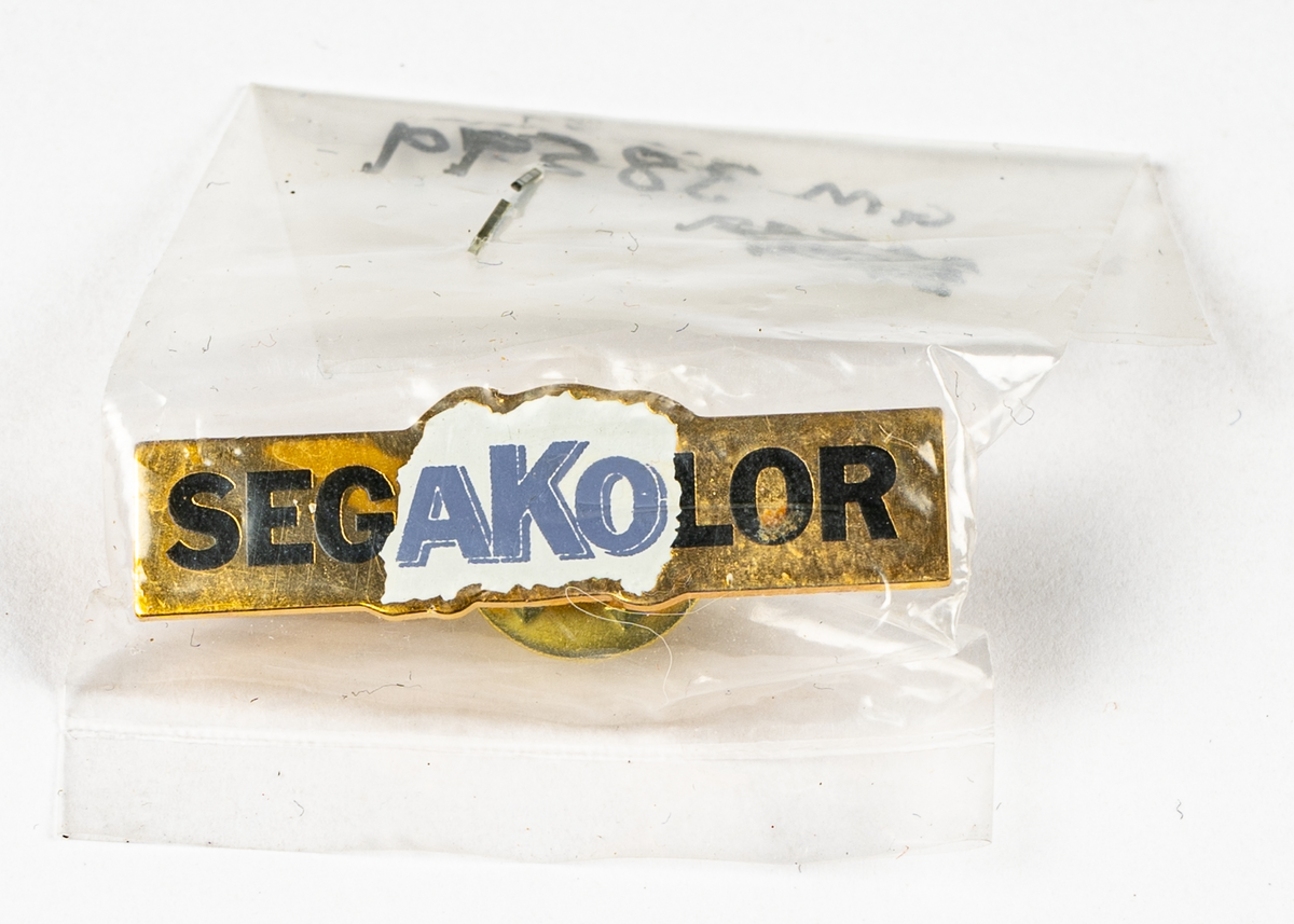 Liten pin i gulmetall med text; Sega AKO kolor, i plastpåse.