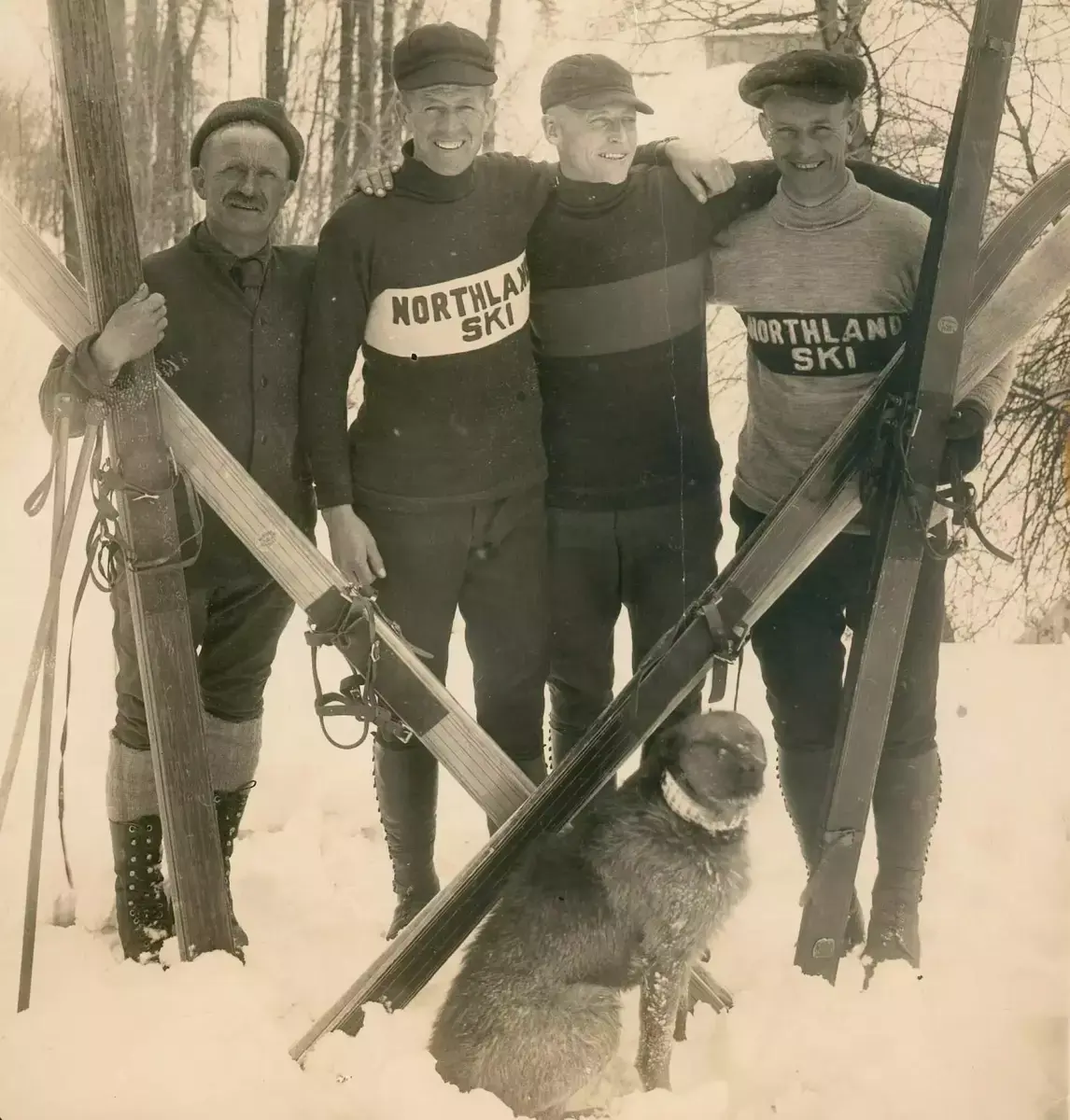 Fire skihoppere i vinterklær. luer og kraftige treski, poserer sammen med hund