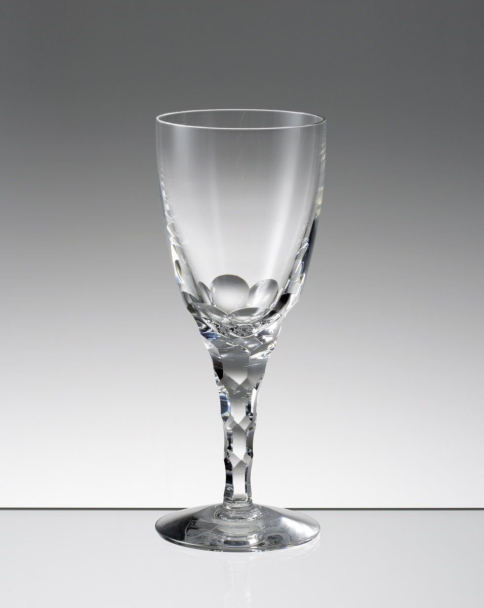 Design: Ingeborg Lundin.
Vitvinsglas. Tulpanformad kupa med fasettslipad nedre del. Konande ben med fasettslipade fjäll.
