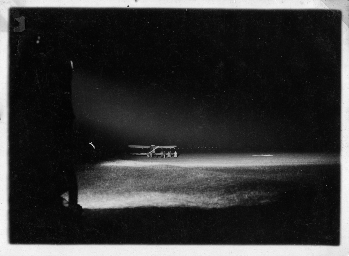 Nattflygning i Rinkaby, 1925.
Klargöring av militärt flygplan på flygfält inför mörkerflygning för Flygkompaniet. Militärer i rörelse vid flygplanet.