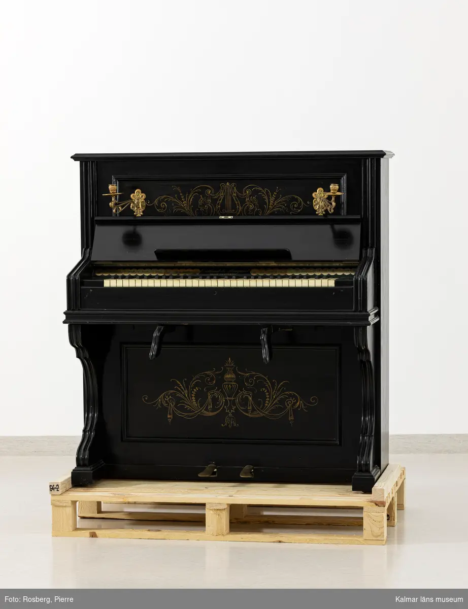 KLM 28771. Orgel, orgelharmonium. Av svartmålat trä med målad dekor i guldfärg. På framsidan två ljusarmar av mässing. 5 oktaver. Ovanför tangenterna text: Östlind & Almquist ARVIKA och GÖTEBORG.