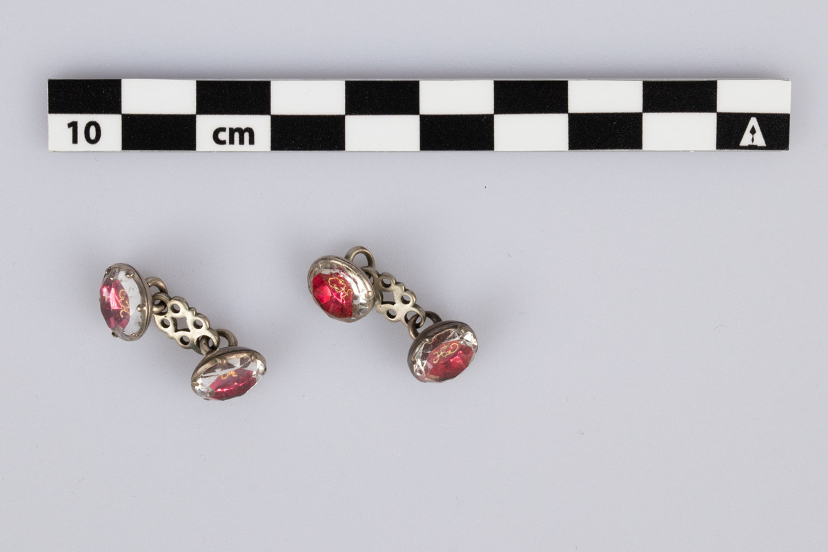 Mansjettknapp med to runde, røde glassknapper med monogram i gullfiligrans, Kort sølv lenke imellom.