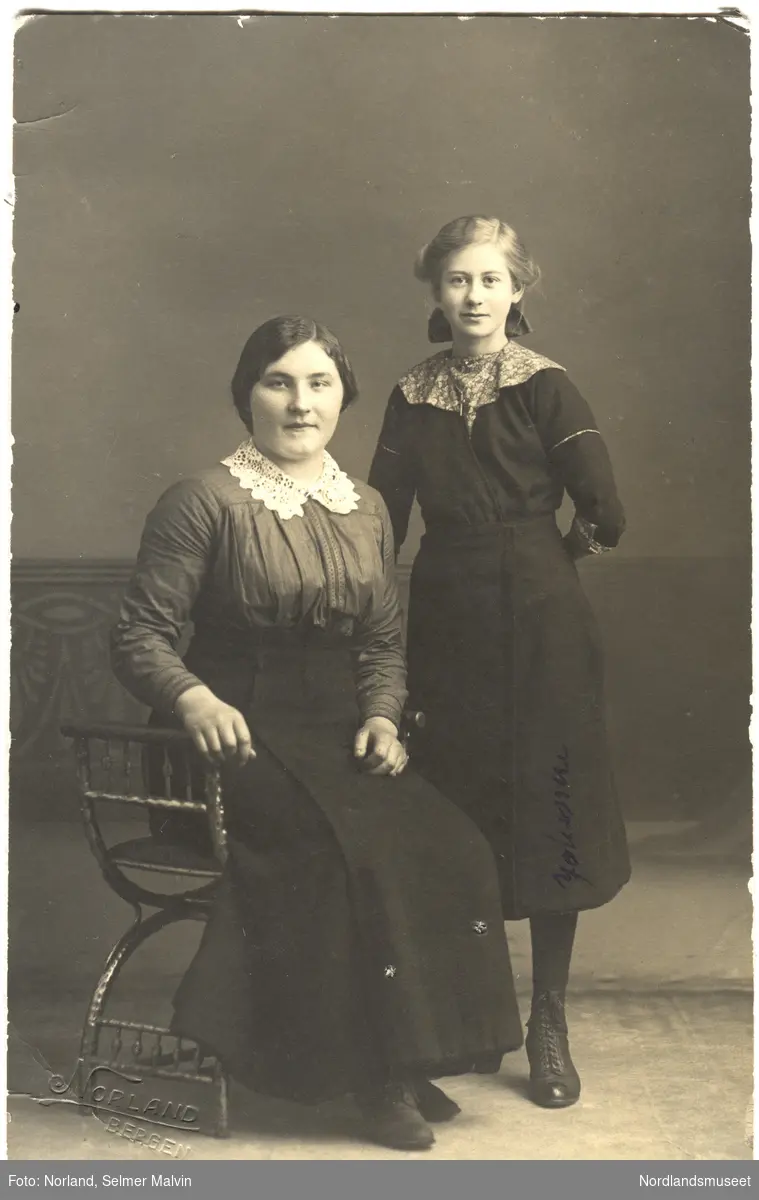 Portrett av to jenter, en sittende på en krakk, atelierbilde, malt bakgrunn