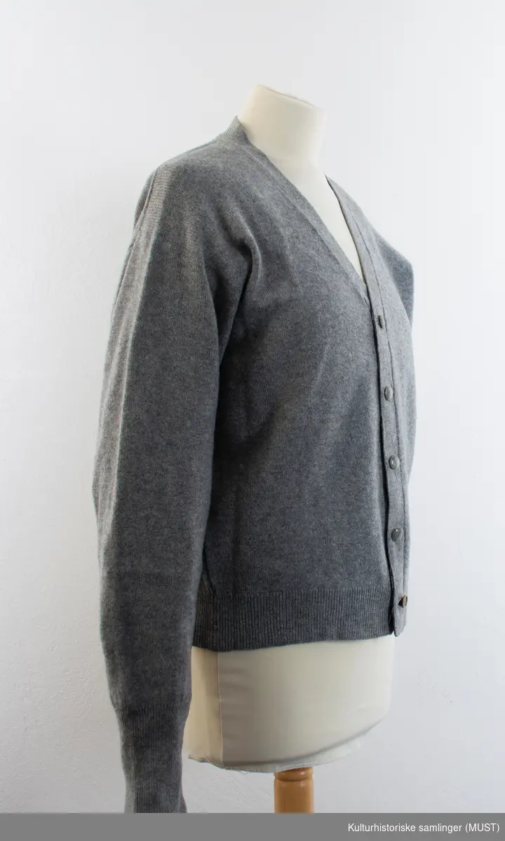 Strikkejakke i grå tynn ull, med V-hals og knappestolpe med fem gråknapper.