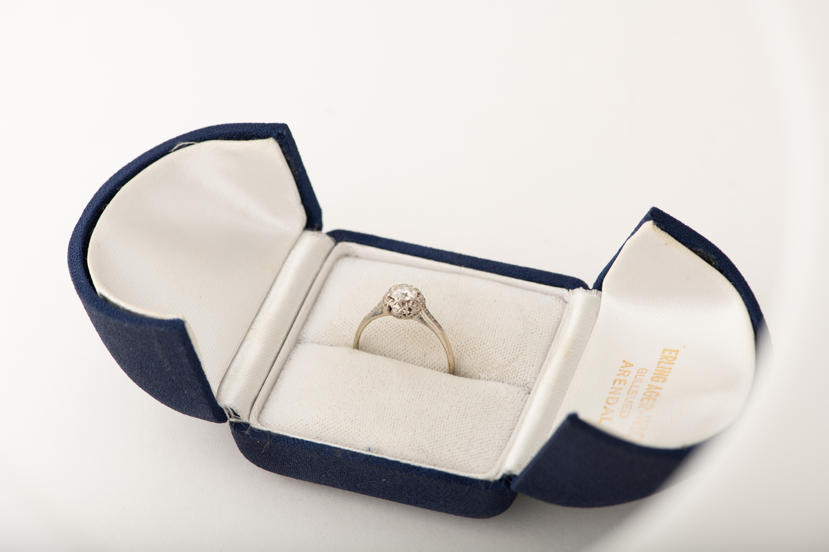 Tynn ring av hvitt gull, stemplet med 585 og vikingskip. Ring med komplisert mønstret fatning, med briljantslipt 6 mm diamant omgitt av splinter og spineller.
