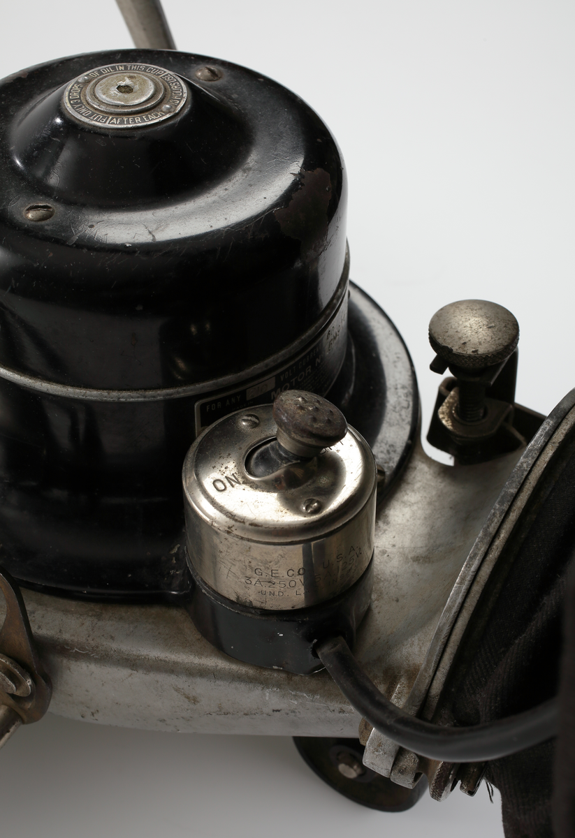 Elektrisk dammsugare av märket The Hoover, tillverkad i USA mellan åren 1923-25. Dammsugaren består av ett sugmunstycke på fyra mindre hjul och med roterande borste. Motorn är placerad ovanpå munstycket. Från sugmunstycket leder ett fällbart/ledat skaft samt en monterad textil dammsugarpåse som går att lossa och haka av vid tömning.