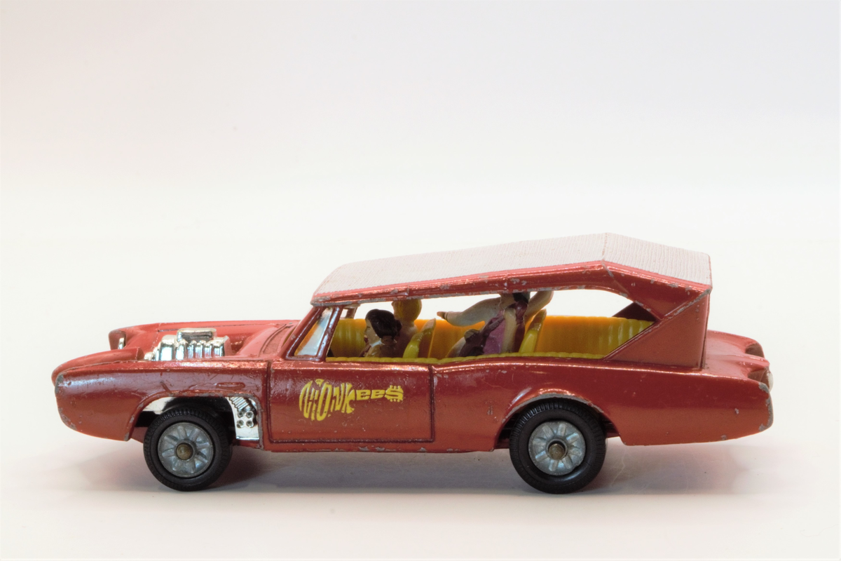 Rød lekebil fra 60/70-tallet. Produsert i Wales. The Monkeemobil. Modell av Dean Jeffries 1966 Pontiac GTO som var med i den amerikanske TV-serien The Monkees. Fire figurer i setene som spiller gitar og vinker, karakterene i serien spiller i band.