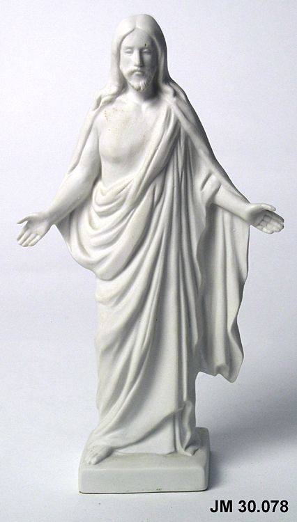Skulptur av vitt gips föreställande Jesus med fotsida dräkt och mantel, och utsträckta armar.