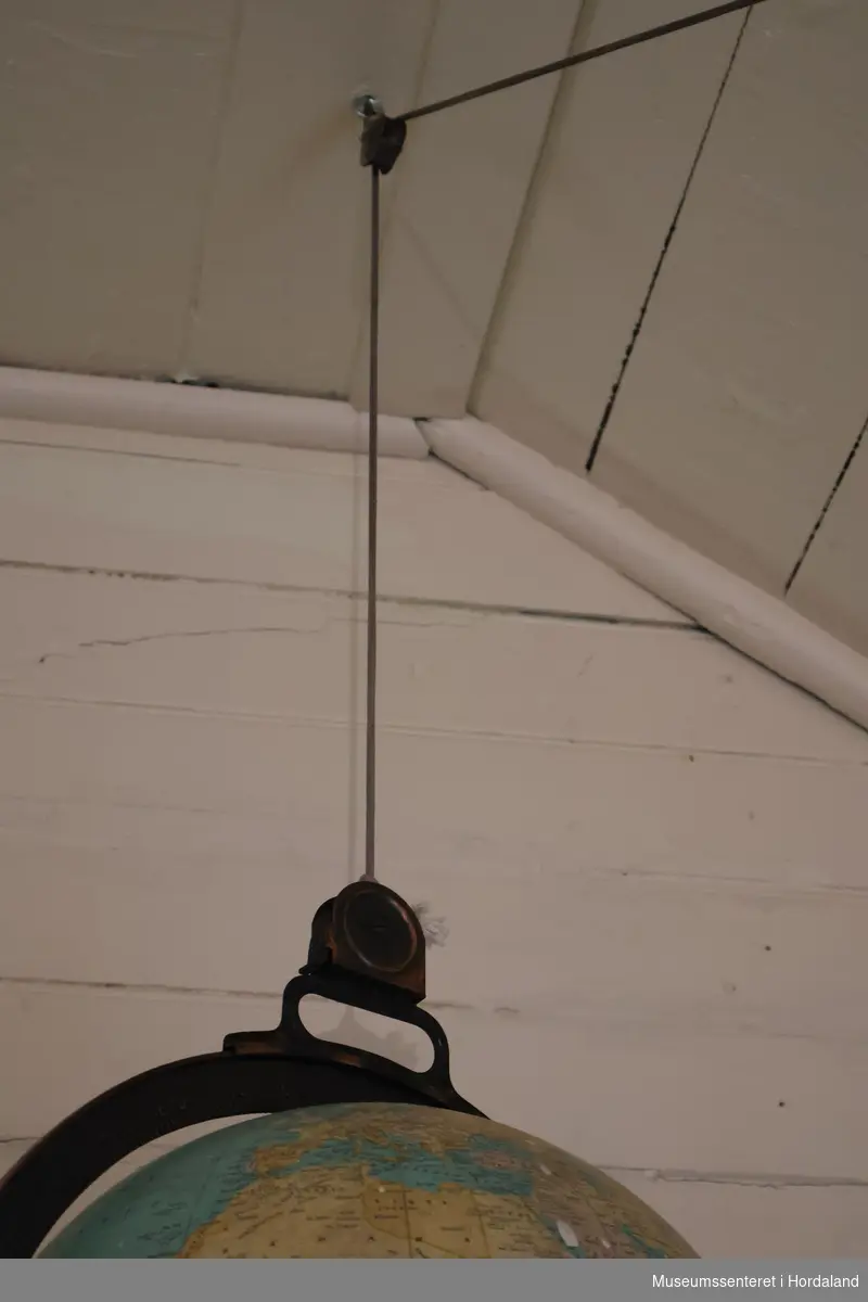 Globus med en ring av metall rundt som har grademål. Globusen henger fra taket i en snor som er trukket gjennom trinse i tak og på vegg, med et kulerundt lodd i enden ved gulvet.
