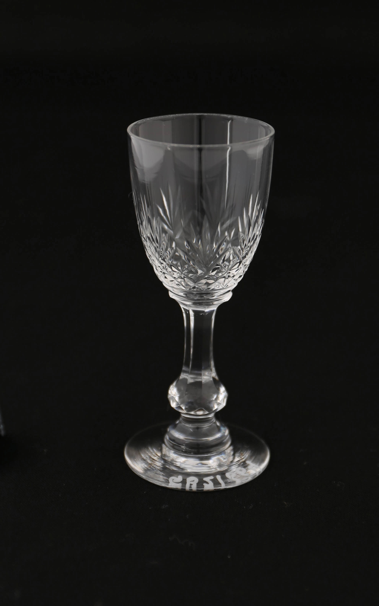 Brennevinsglass av glass med fasettert stett med vulst på rund fot, samt slipt strek-dekor på klokke.