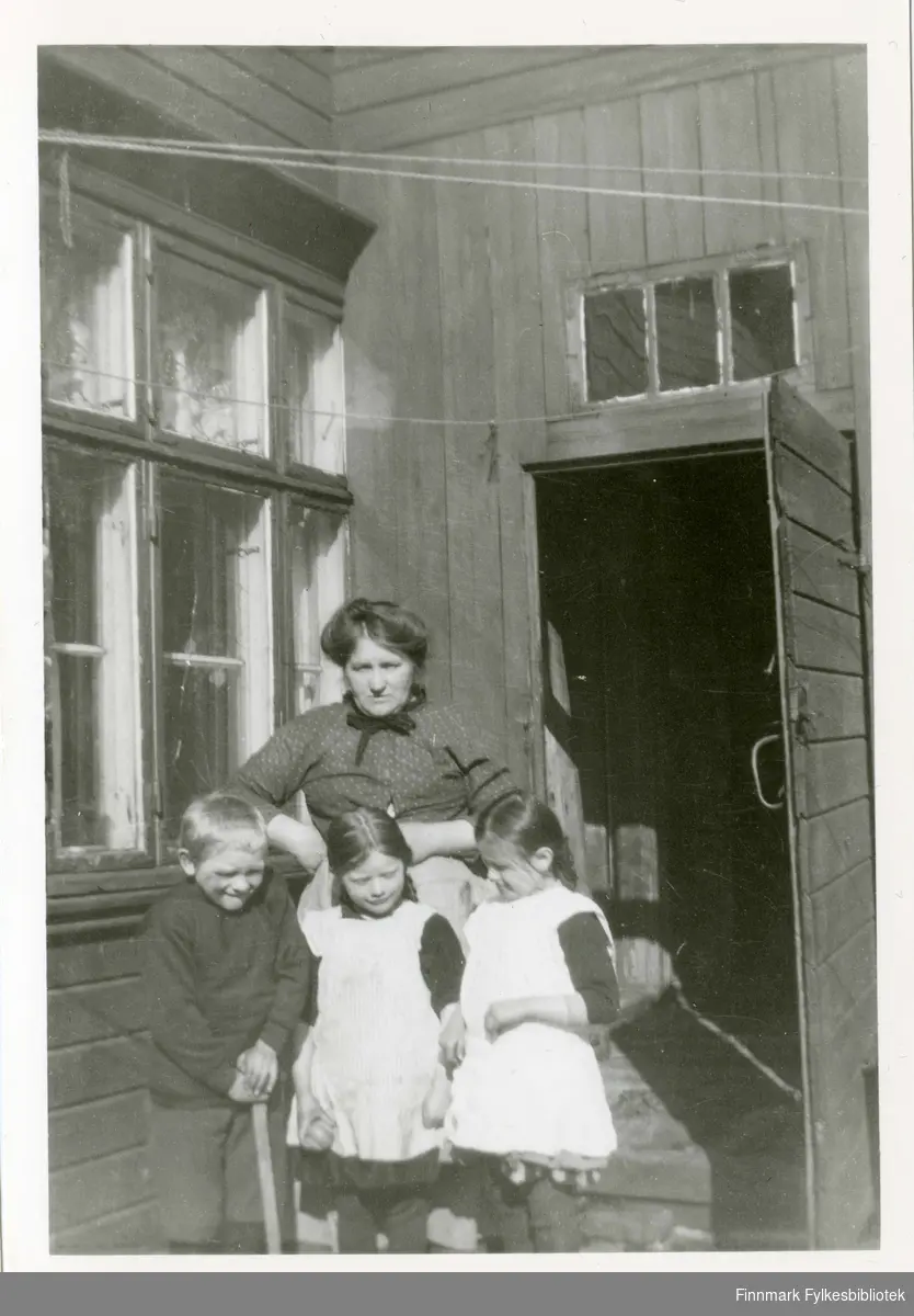 Jensine Alexandersen med barna Einar, Alfild og Else, Hammerfest. I bakgården, utenfor kjøkkenvinduet og kullageret. 