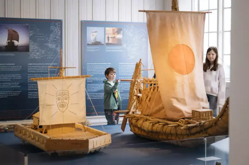 To barn kikker på modeller av seilbåter. Gutten på bildet peker opp på båten.